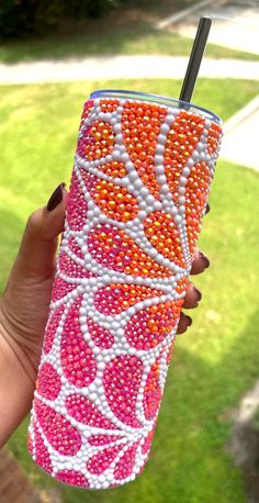 a hand holding a pink and orange cup with beaded designs on the outside, in front of a grassy area