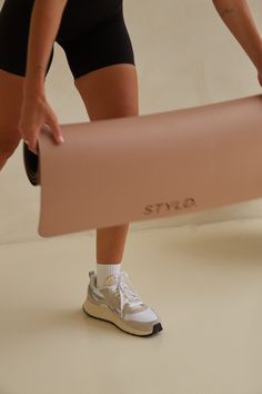 a woman holding a yoga mat in her right hand and wearing white tennis shoes on the other