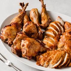 a white plate topped with sliced chicken next to a fork and knife on top of a table