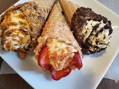 three ice cream cones on a white plate with strawberries and other desserts in them