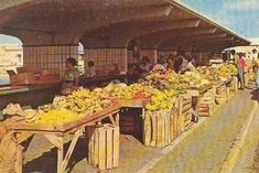 an old photo of people standing at a fruit and vegetable stand with bananas on the tables