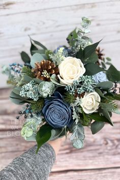 a bridal bouquet with blue flowers and greenery is held by someone's hand