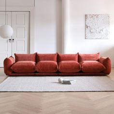 a red couch sitting on top of a wooden floor next to a white rug in a living room