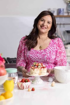 a woman sitting at a kitchen counter holding a cake on a plate with strawberries