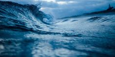 an ocean wave is breaking in front of the shore and trees on the other side