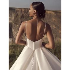 a woman in a white wedding dress looking out at the ocean and cliffs with her back to the camera