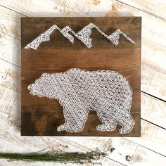 the bear is made out of string and sits on a wooden board with mountains in the background