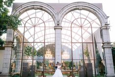 a bride and groom standing in front of an arched glass building with chandeliers