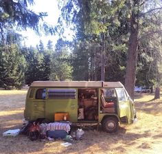 an old vw bus parked in the woods with its doors open and luggage piled up