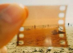 a person holding up a polaroid photo on the beach with people in the background