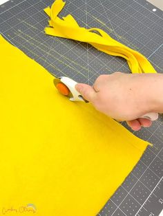 someone is cutting fabric with scissors on a yellow piece of paper that has been cut into smaller pieces