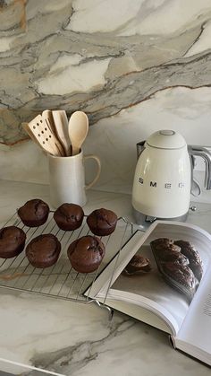 there are chocolate muffins on the rack next to an open book and coffee pot