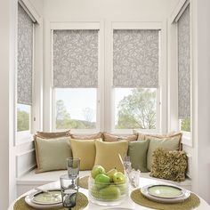 a white table topped with green plates and bowls filled with fruit next to two windows