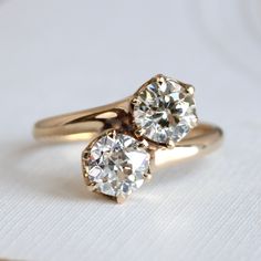 two diamond engagement rings sitting on top of each other, one is yellow gold and the other is white gold