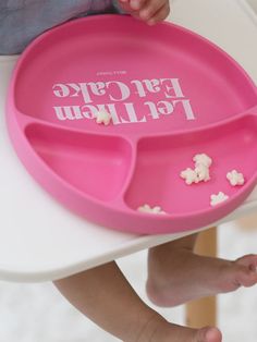 a child's hand holding a pink plate with popcorn on it