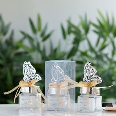 two small glass jars with butterfly decorations on them sitting on a table next to some plants