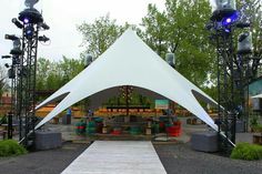 an outdoor stage set up with white tents and lights on the sides, surrounded by trees