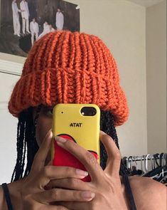 a woman taking a selfie with her cell phone wearing an orange knitted hat