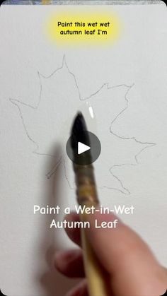 a person holding a paintbrush in their left hand and drawing on the wall with an autumn leaf