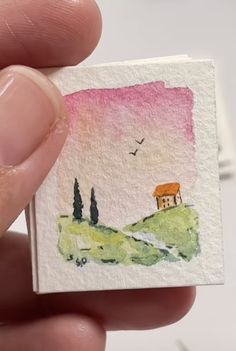 a hand holding a small piece of paper with a painting on it