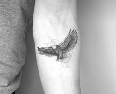 a black and white photo of a bird tattoo on the left arm, with an eagle flying above it