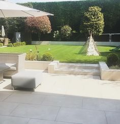 an outdoor patio with white furniture and umbrellas on it's sides, surrounded by greenery