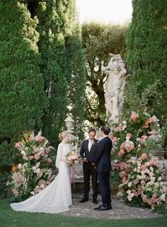 a bride and groom standing in front of an arch with flowers on it, surrounded by greenery