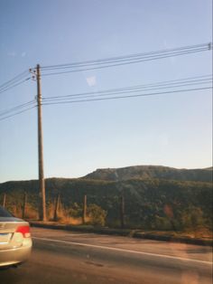 a car is driving down the road with power lines in the back ground and hills behind it