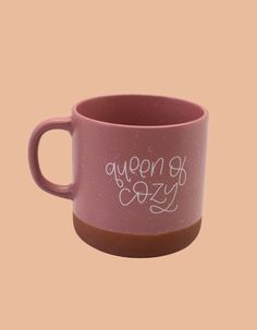 a pink coffee cup with the words queen of cozy written in white ink on it