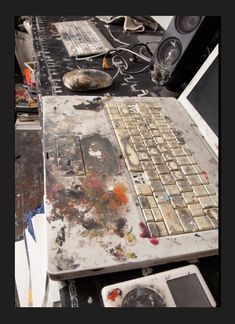 an old laptop computer sitting on top of a table covered in paint and other junk