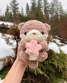 a hand holding a teddy bear with a pink heart on it's chest in the snow