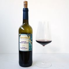 a bottle of wine next to a glass filled with red wine on a white table