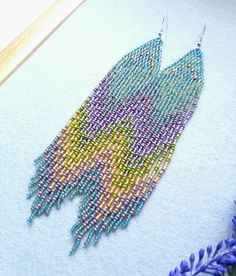 a pair of beaded earrings sitting on top of a piece of paper next to purple flowers