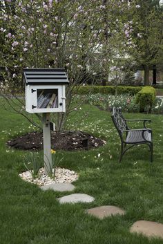 a bird house sitting on top of a lush green field next to a park bench