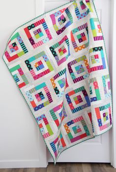 a multicolored quilt hanging on the side of a white door with wood flooring