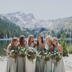 a group of women standing next to each other in front of a lake with mountains