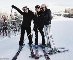 three people on skis posing for the camera with their arms in the air and one person holding two ski poles