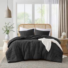 a bed with black comforter and pillows in a room next to a wicker basket