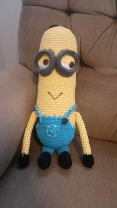 a crocheted minion with glasses sitting on a couch next to a chair