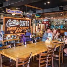 people sitting at tables in a restaurant with signs hanging from the ceiling and wooden chairs around them