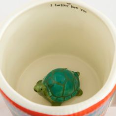 a ceramic turtle sitting in a cup with writing on the bottom and inside it's lid