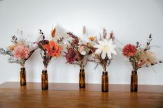 five brown vases with flowers in them on a wooden table next to a white wall