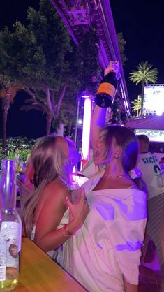 two women standing next to each other in front of a bar with purple light on it