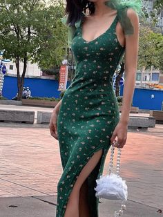 a woman in a green dress is holding a white purse and posing for the camera