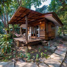 a small cabin in the woods with a porch and hammock hanging from it's roof