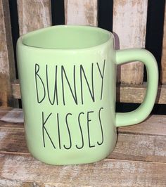 a green coffee mug with the words bunny kisses on it sitting on a wooden bench