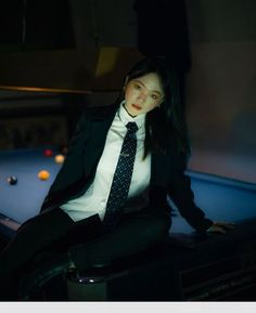 a woman in a suit and tie sitting on a pool table