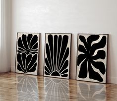 three black and white art pieces sitting on top of a hard wood floor next to a window