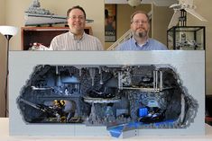 two men standing next to each other in front of a model of a space station