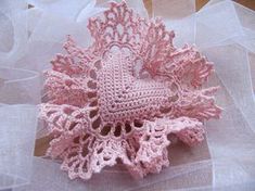 a pink crocheted object sitting on top of a white net covered table cloth